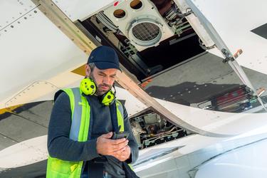 aircraft turnaround maintenance guy on the tarmac checking his ruggedised smartphone under the plane aircraft turnaround maintenance guy on the tarmac checking his ruggedised smartphone under the plane