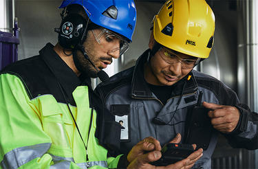 Two helmeted industry workers looking at smart device Two helmeted industry workers looking at smart device