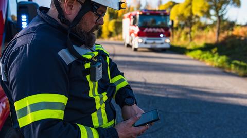 Fireman looking at his smartphone displaying Agnet user interface next to a fire truck and forest