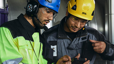 Two helmeted industry workers looking at smart device