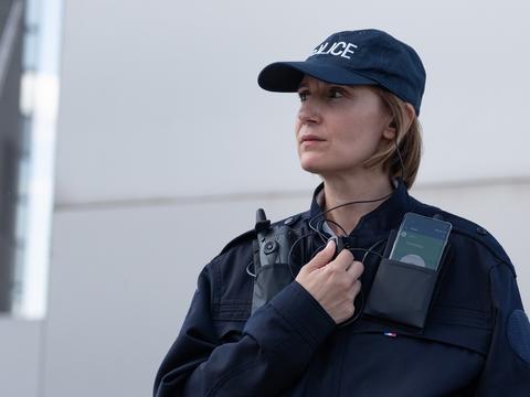 Police woman equipped with radio device and smartphone displaying Agnet using PTT accessory