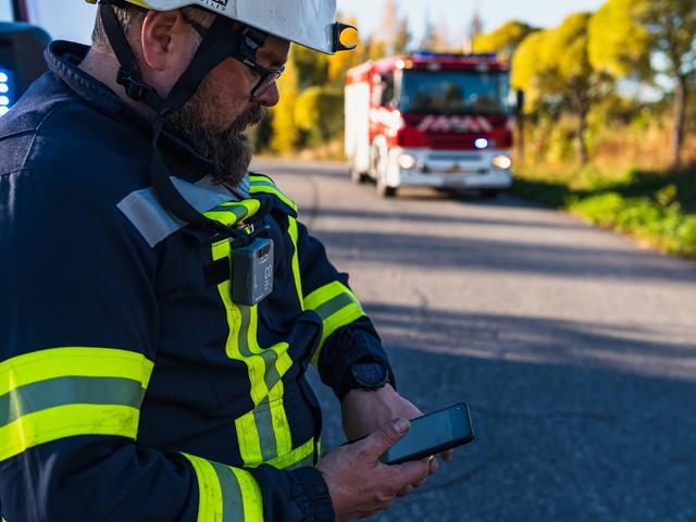 Fireman looking at his smartphone displaying Agnet user interface next to a fire truck and forest
