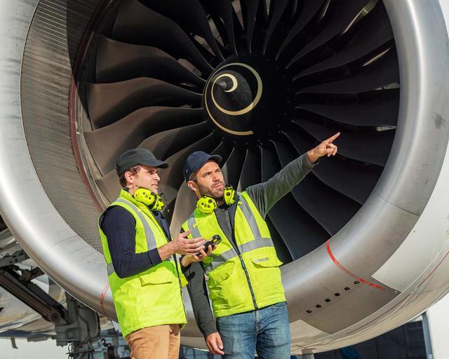 Ground handlers discussing in front of a airplane jet engine Ground handlers discussing in front of a airplane jet engine