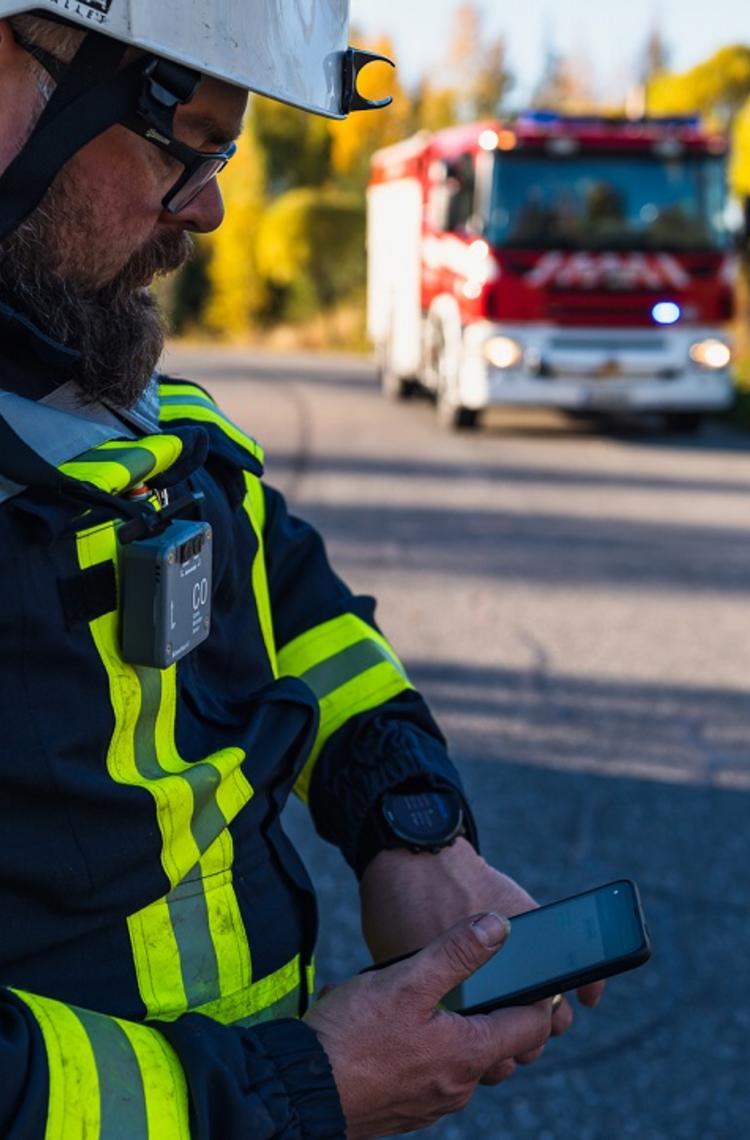 Fireman looking at his smartphone displaying Agnet user interface next to a fire truck and forest Fireman looking at his smartphone displaying Agnet user interface next to a fire truck and forest
