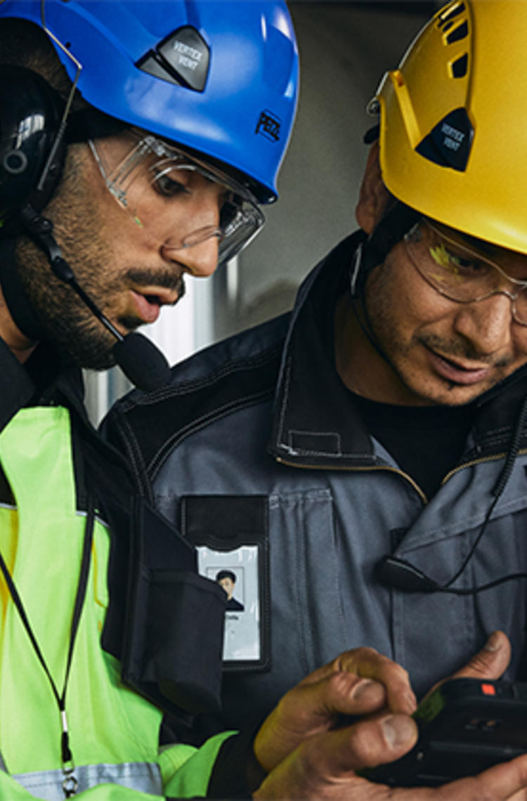 Two helmeted industry workers looking at smart device Two helmeted industry workers looking at smart device