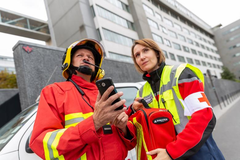 Fireman holding smartphone and paramedic woman holding medipack looking offscreen