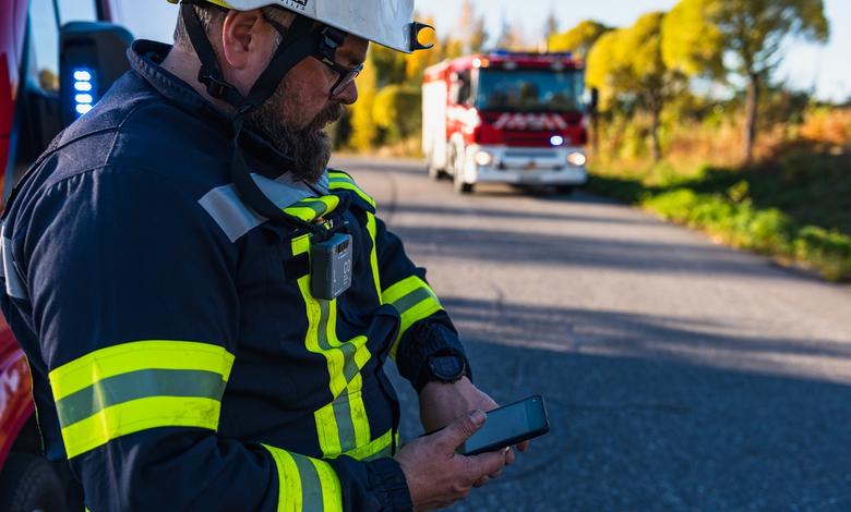 Fireman looking at his smartphone displaying Agnet user interface next to a fire truck and forest