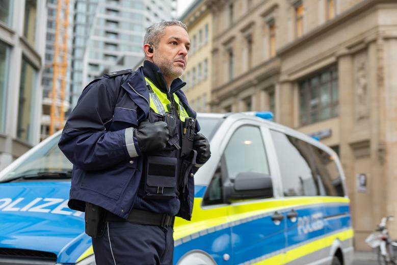 Policeman equipped with ruggedized smartphone and PTT accessory watching in the street next to a police car