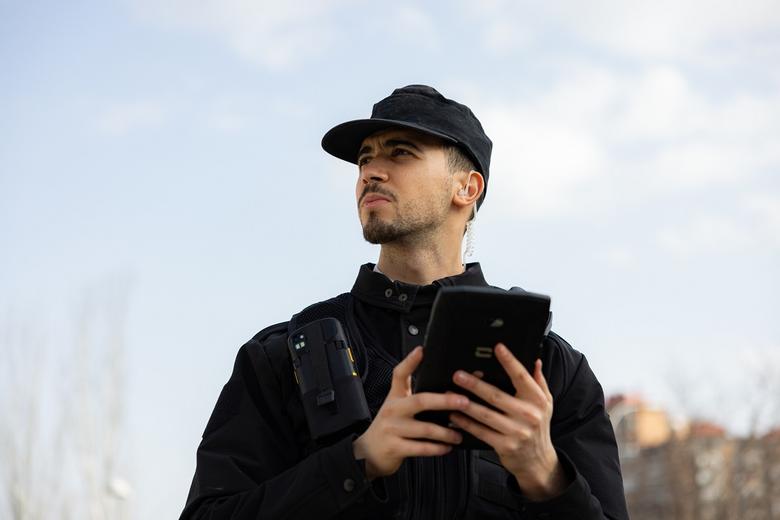 Security guy equipped with ruggedized smartphone and tablet watching in the city