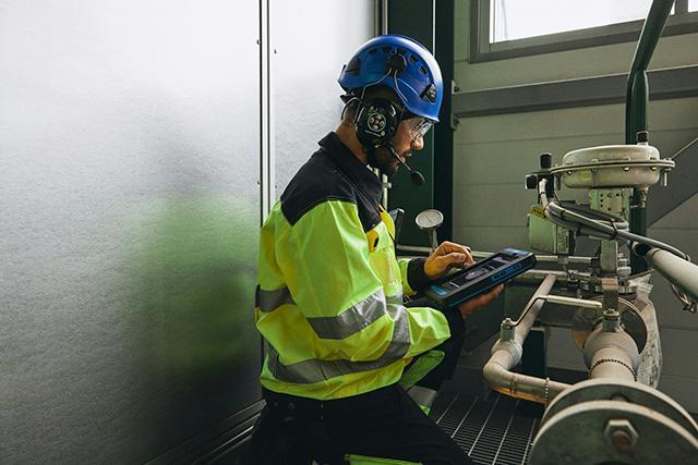 Worker with smart device next to factory equipment