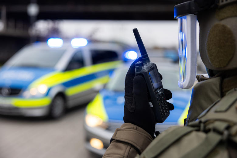 Swat officer talking to a TPH900 Tetrapol terminal with police cars on the background